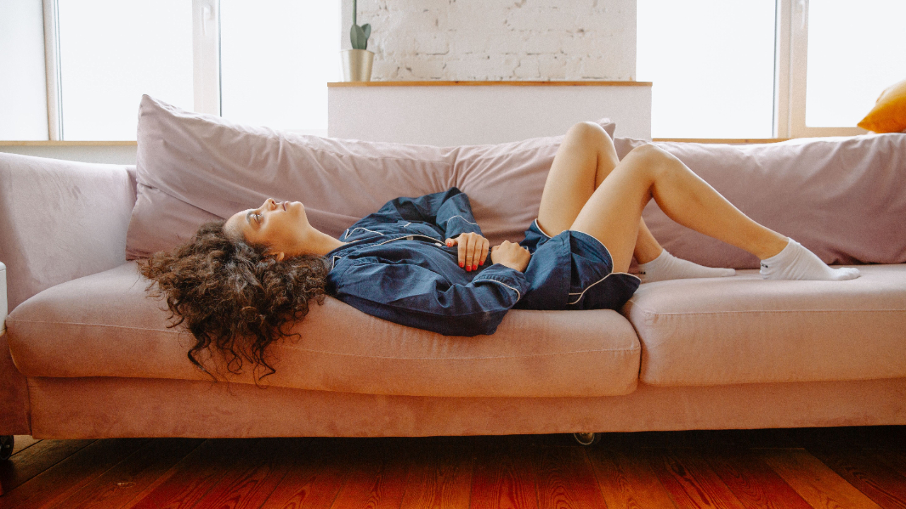 oman lying on a sofa in discomfort, hand resting on her stomach, illustrating pelvic and sexual pain discussed in Intimata's vaginismus and dyspareunia guide