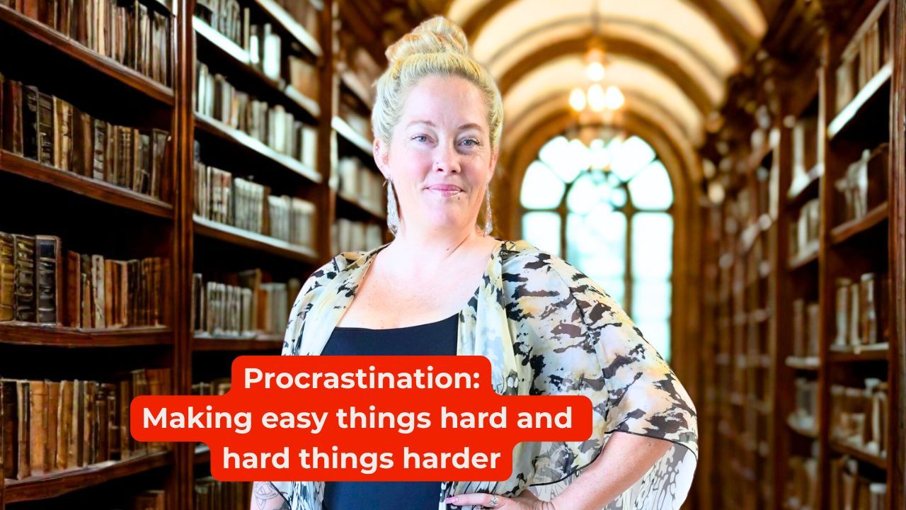 Woman in black shirt and a floral shawl smiling with her hands on her hips with words on the screen that say, "Procrastination: Making easy things hard and hard things harder"