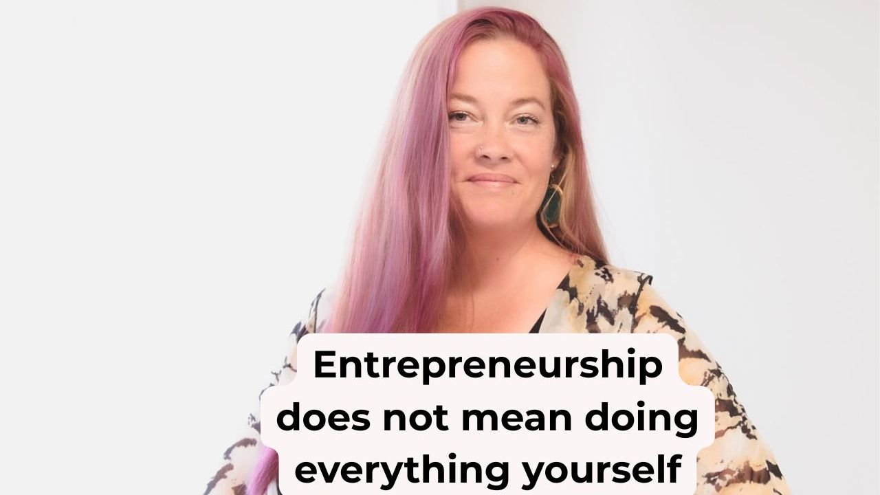 Woman in pink hair in a floral shawl smiling with words on the screen that say, "Entrepreneurship does not mean doing everything yourself"