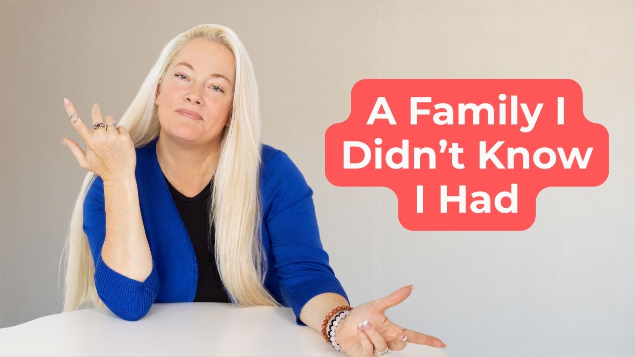 Woman in black shirt and royal blue blazer with her hands gesturing in opposite directions, one up and one down, with words on the screen that say, "A Family I Didn't Know I Had"