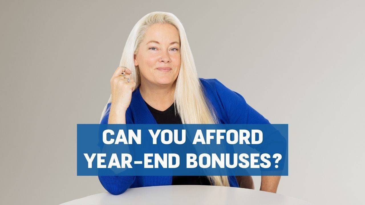 Blonde woman sitting at a white round table smiling with one hand on her hip and the other arm bent with the elbow on the table and words on the screen that say"Can You Afford Year-End Bonuses"