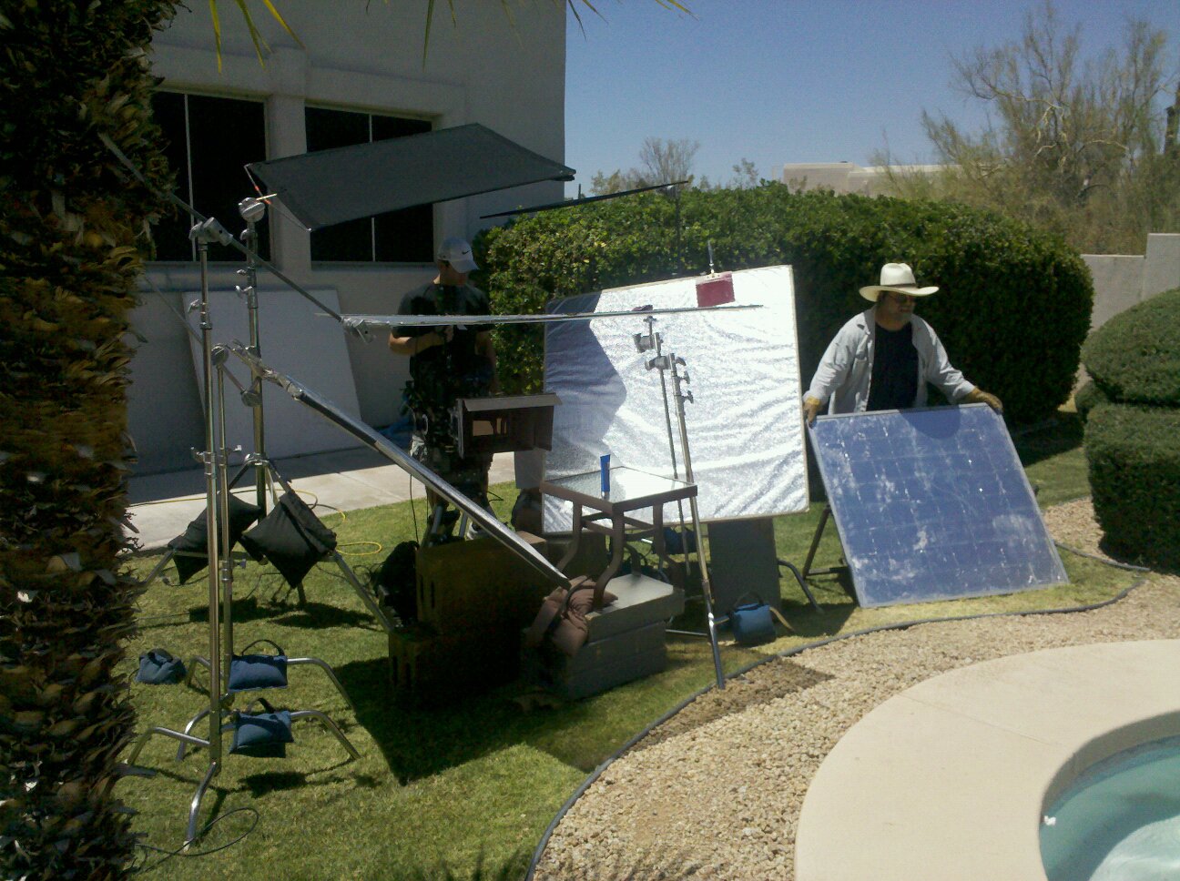 Poolside commercial setup with overhead diffusion and large reflectors for the product and background talent