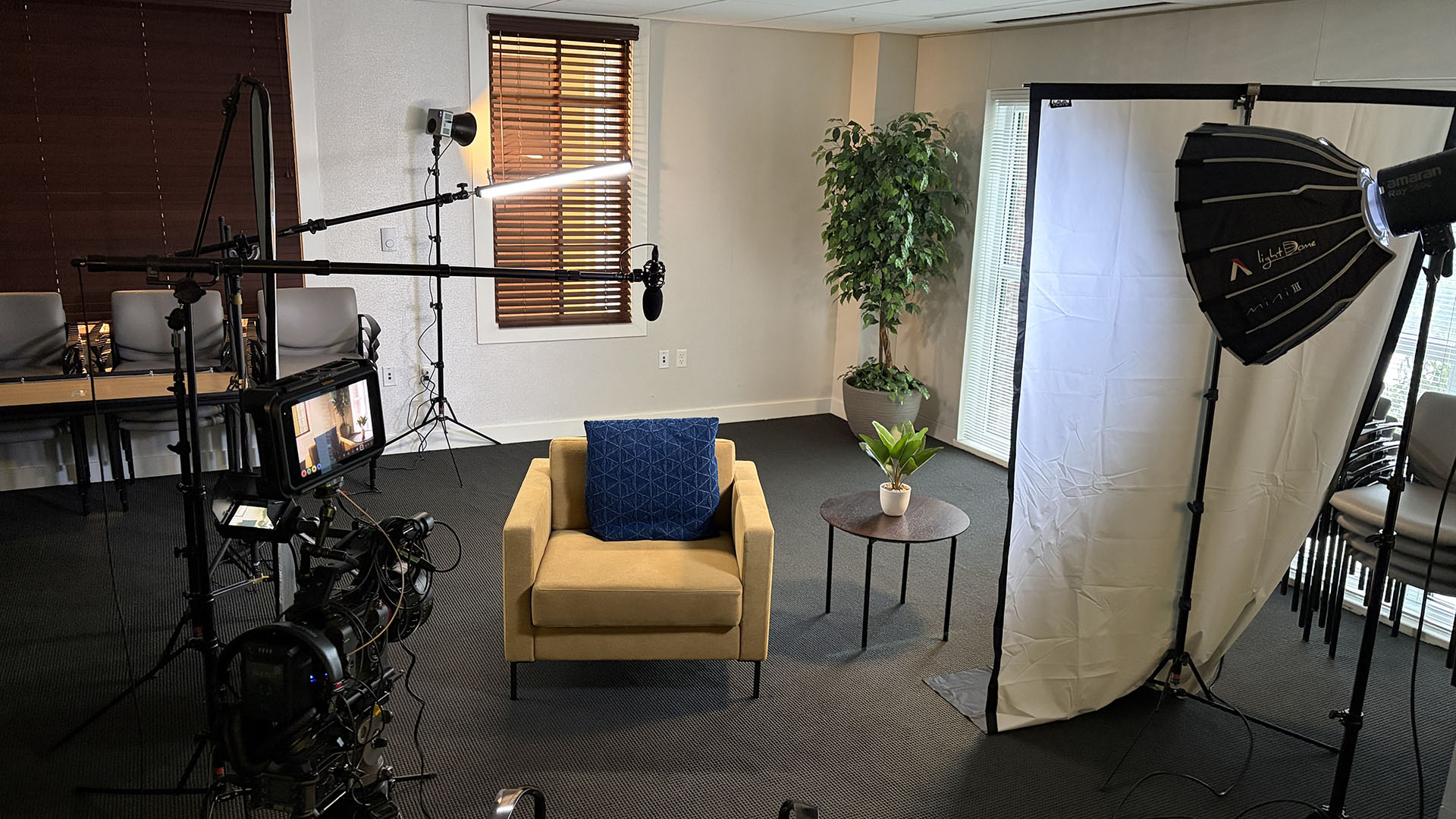 Wide behind-the-scenes view of the interview set with the chair, key light, flags, and background