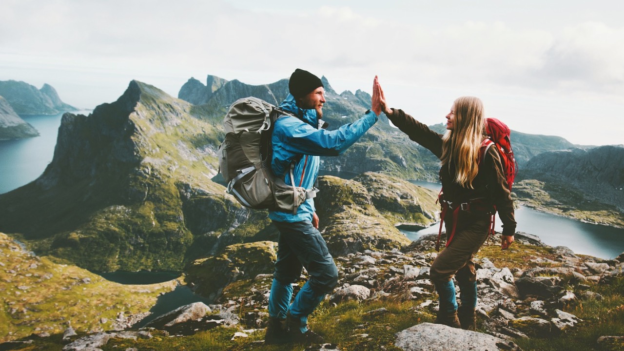 Two adventure guides, one man and one woman, high-five on a mountain summit.