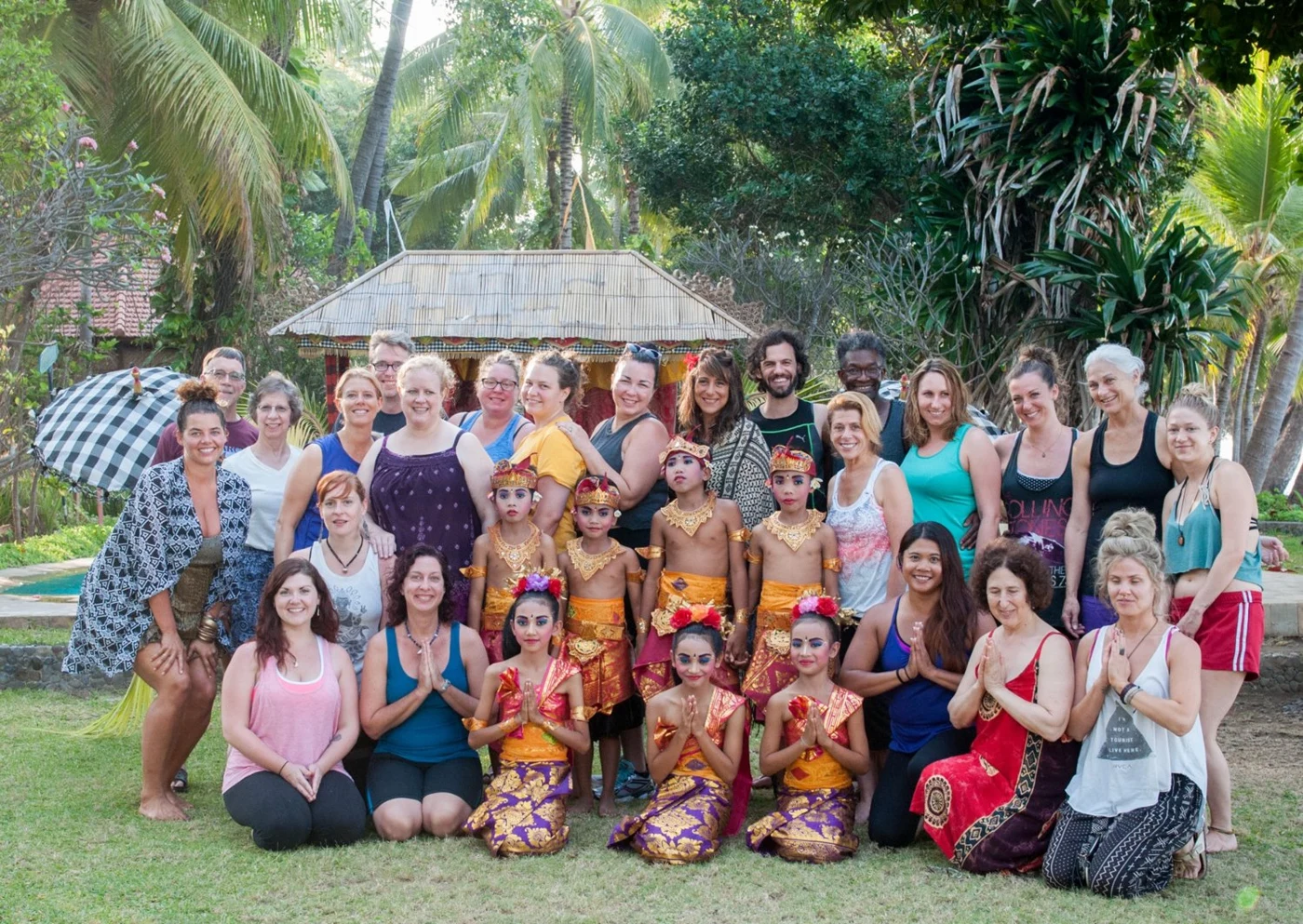 Retreat participants and Balinese performers pose together in a tropical garden at an opening ceremony.