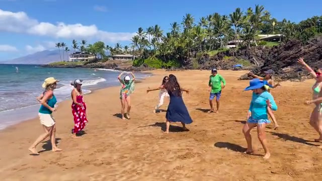 People wearing headphones dance in an open circle beside the ocean.