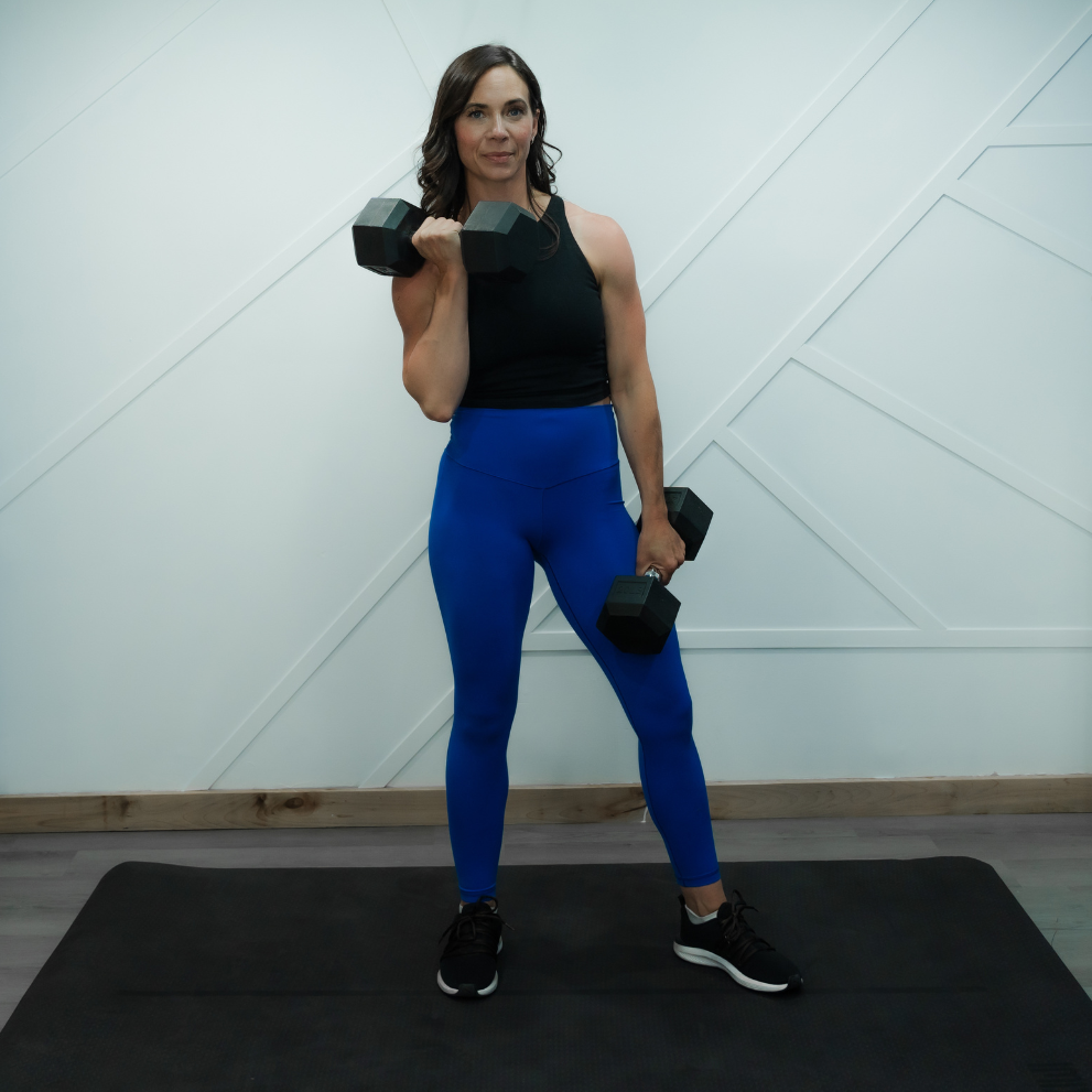 Angela holding one dumbbell at her shoulder and one by her side
