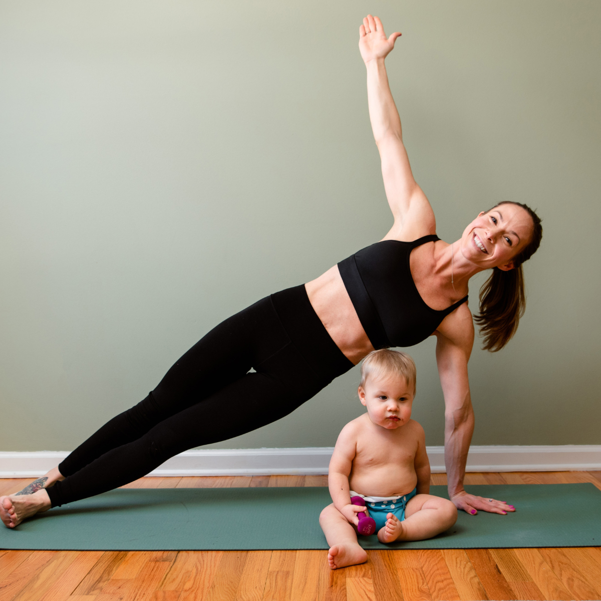 Angela performing a side plank beside her baby
