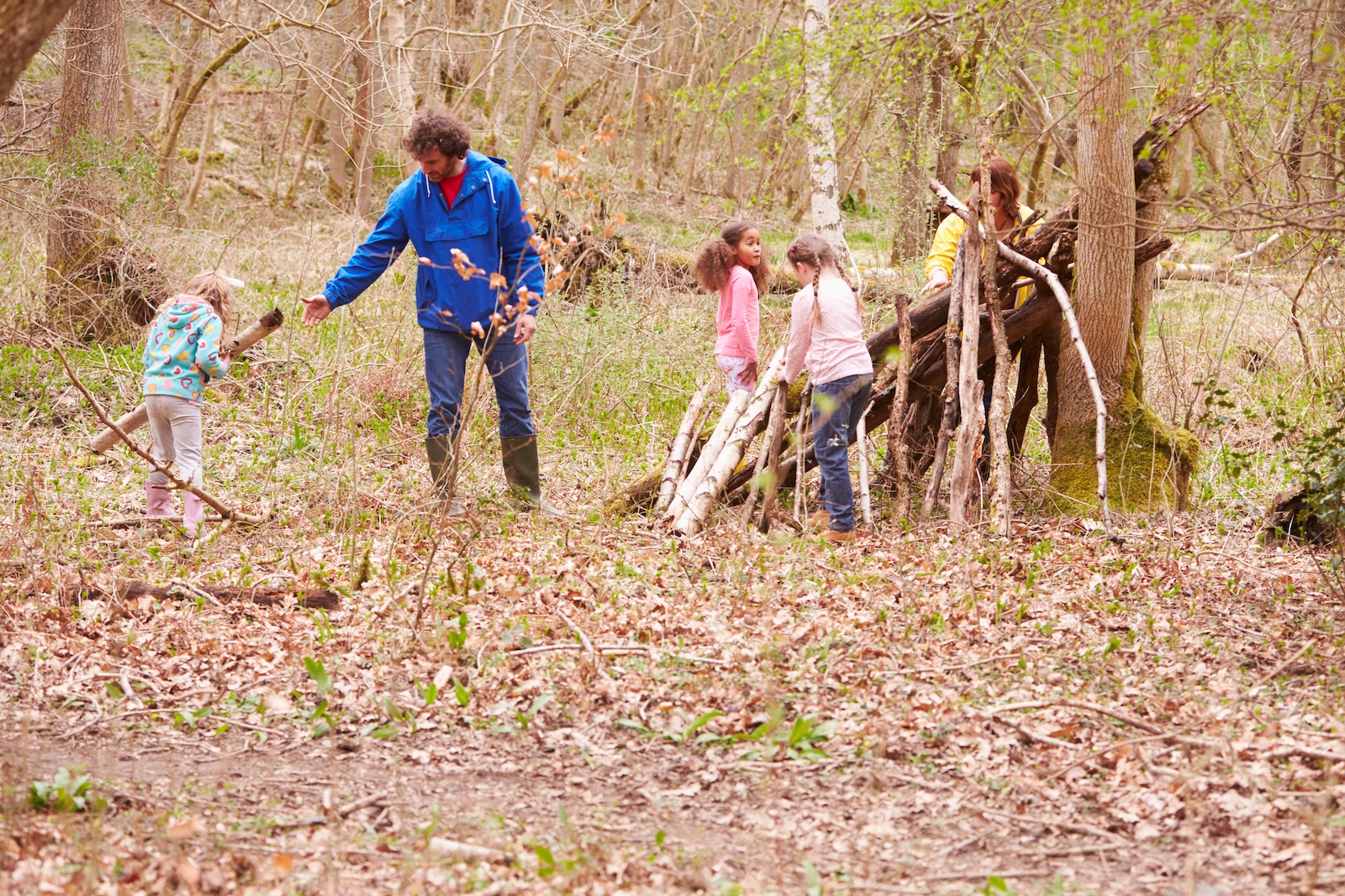 Adult and children building a shelter from branches together in a spring forest