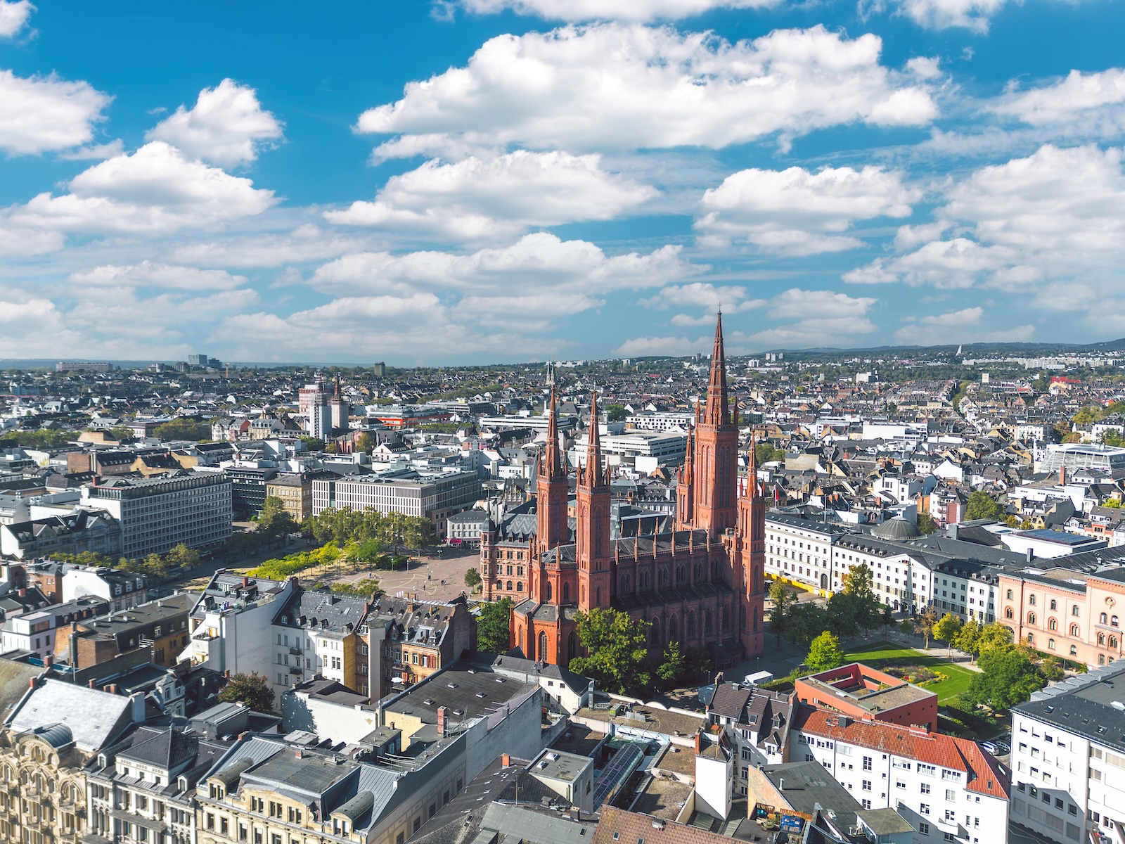 Aerial view of Wiesbaden's red-brick Marktkirche rising above the city center under a blue sky