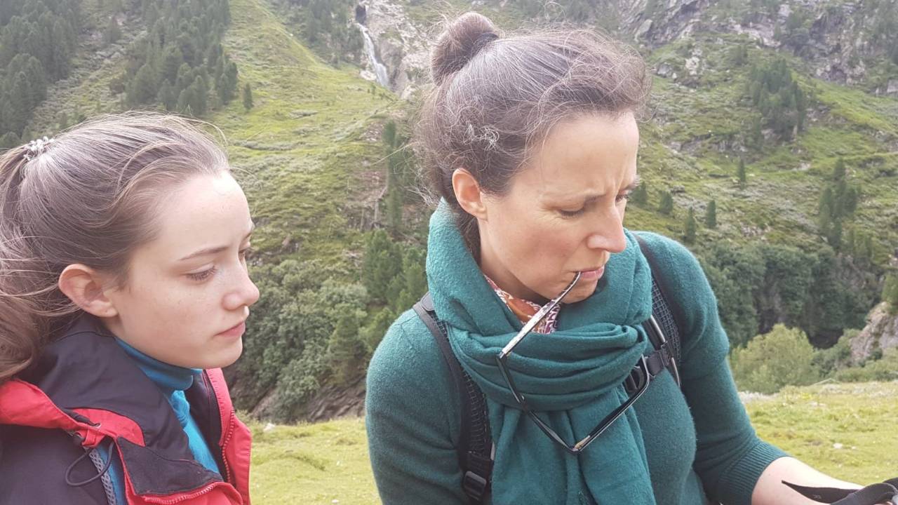 Christine and her daughter hiking in the Alps, with a waterfall and forested slopes behind them