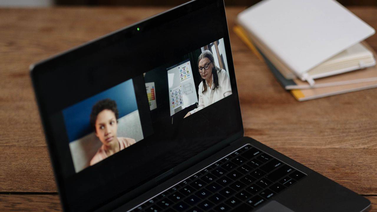 Laptop on a wooden desk showing a video call with two people