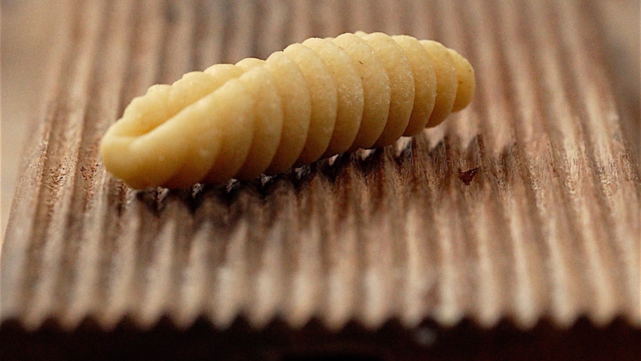 A ridged piece of pasta on a wooden gnocchi board