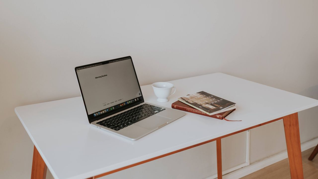 A laptop, cup and notebook on a clean white desk