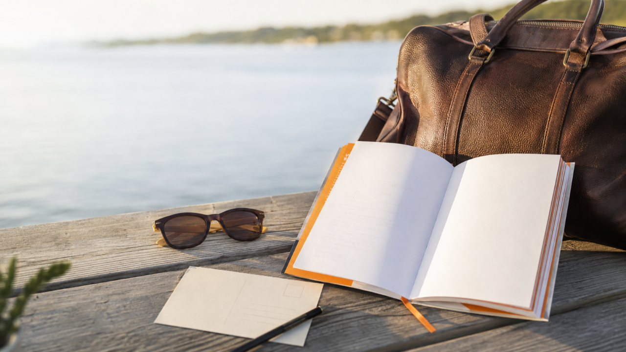 The 10-Year Letter book open beside sunglasses and a travel bag on a wooden dock overlooking calm water.