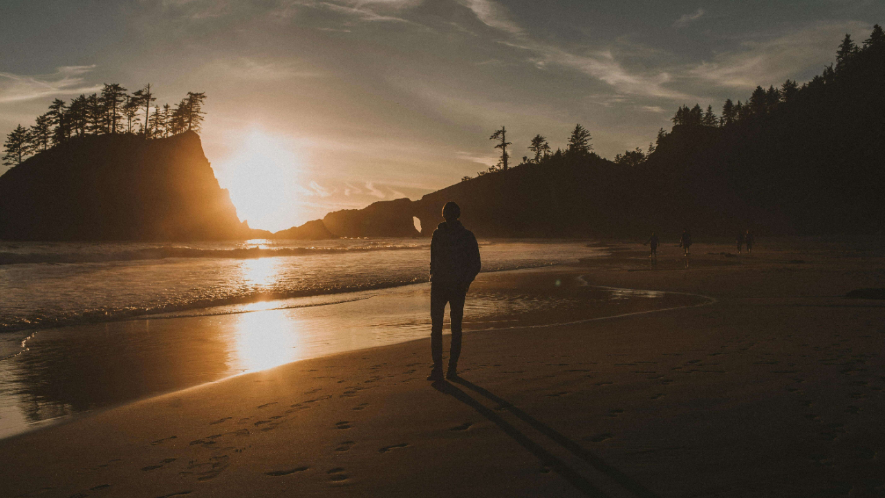 Silhouette of a person standing alone on a beach at sunset with footprints in the sand | expat emotional exhaustion | international therapy and coaching | England | Netherlands