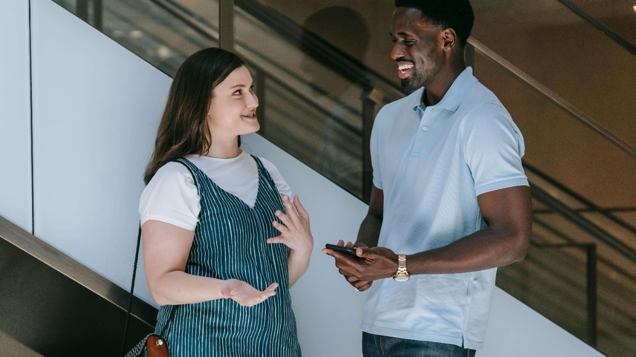 A woman and man laughing and talking together casually in a bright modern building stairwell | globally mobile relationships | international therapy and coaching | expat commitment issues | South Africa | Portugal | England