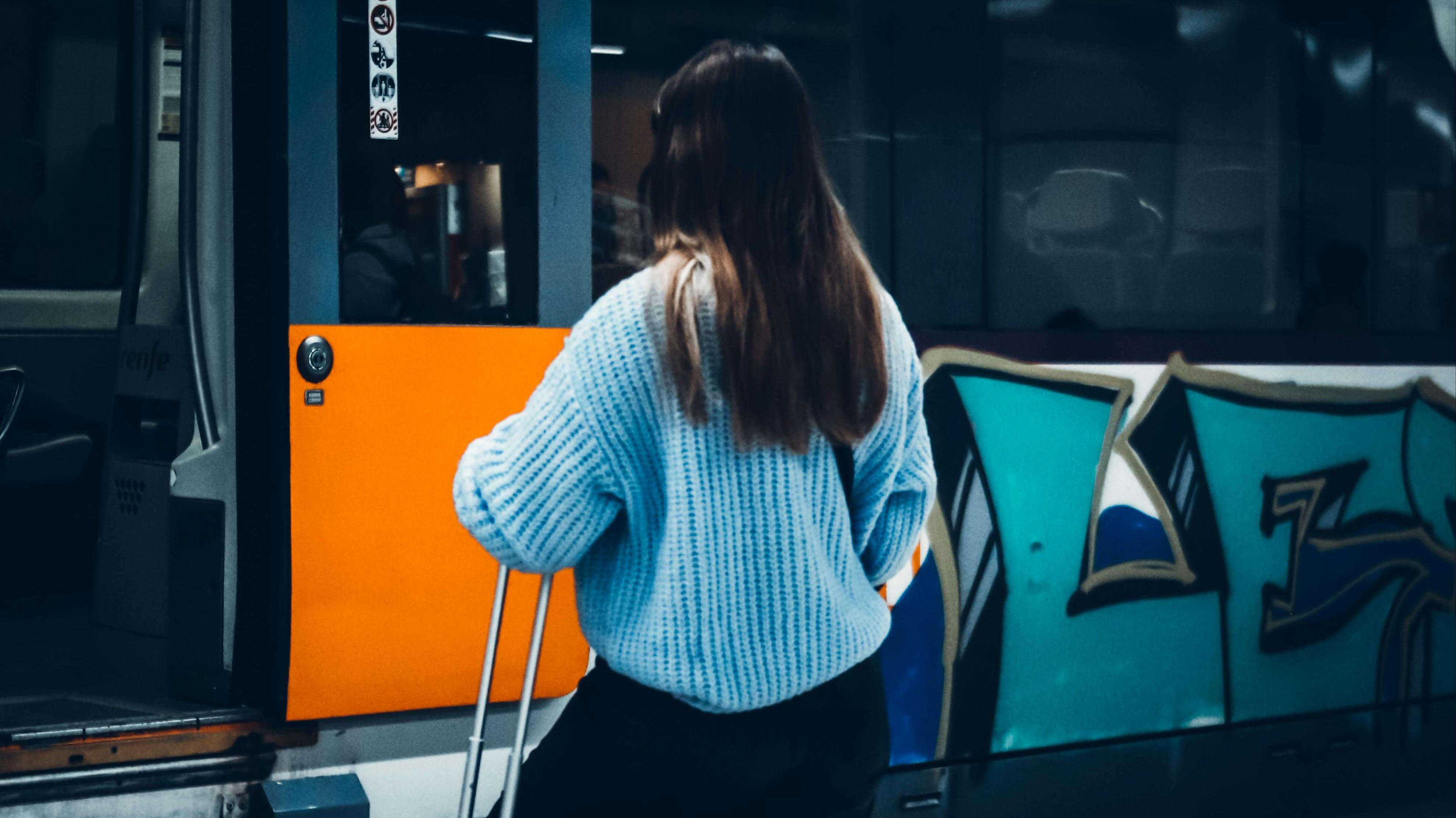 Woman with a rolling suitcase boarding a train at night on a city platform | therapy for expats | living abroad mental health | chronic stress expat | Germany | Portugal | United States