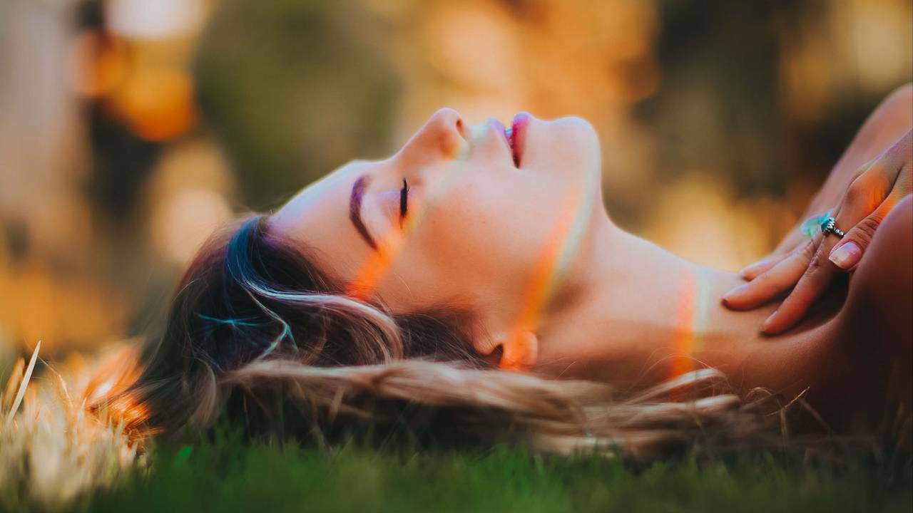 Woman with long blonde hair lying peacefully in the grass with eyes closed in warm golden evening light | energy healing trauma | somatic energy therapy | international trauma therapist | New York City | Chicago | Los Angeles