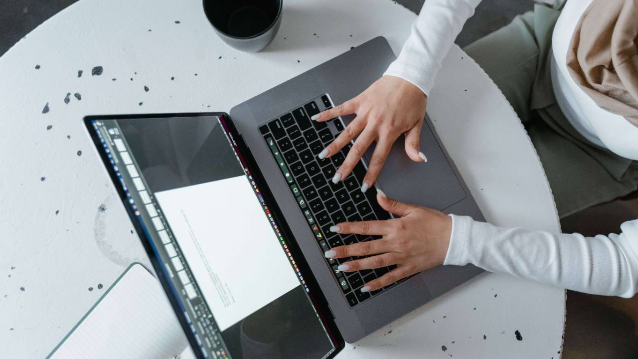 Overhead view of a woman in a white long sleeve top typing on a laptop on a round white speckled table with a black mug beside her | therapeutic coaching online | international trauma therapist | parts work training for therapists | New York City | Chicago