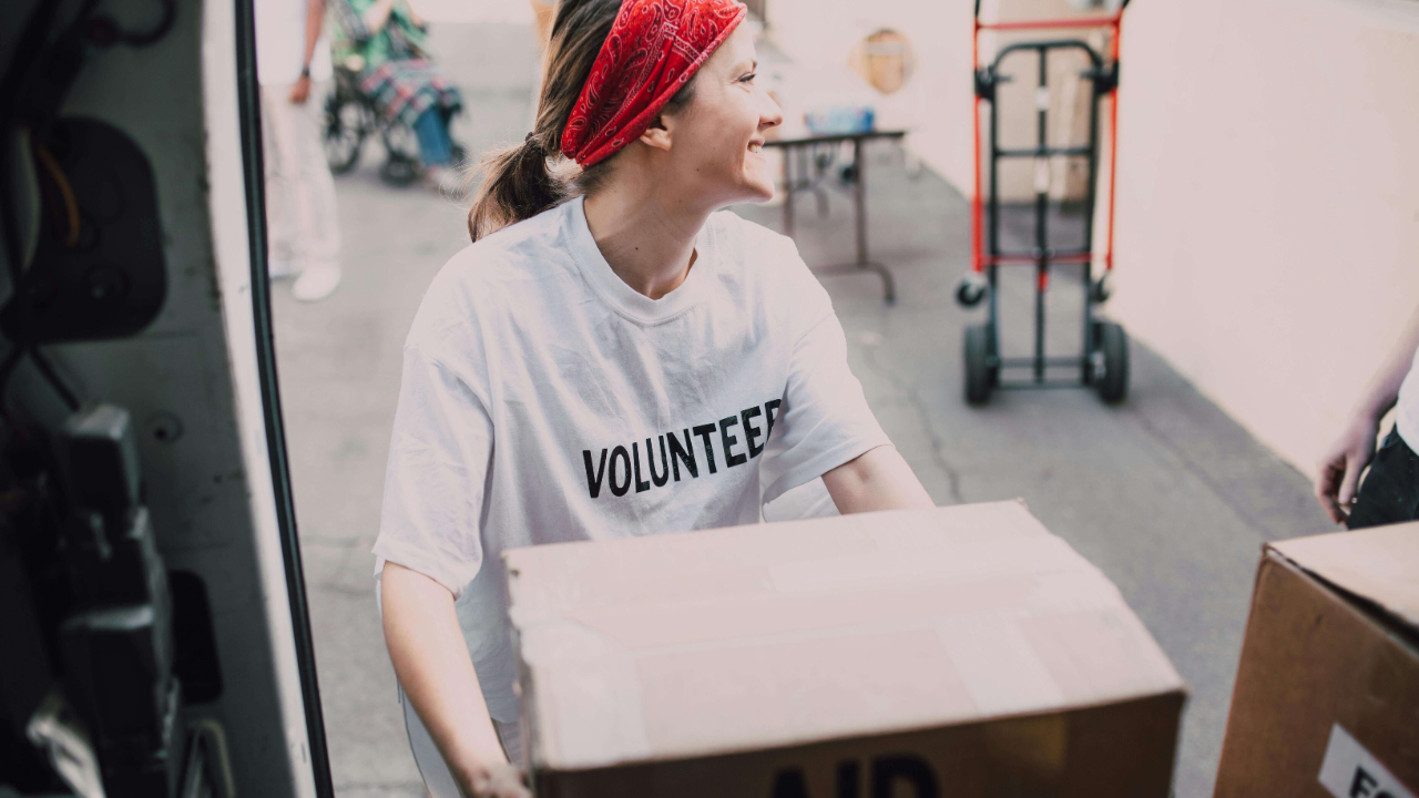 Smiling woman in a volunteer t-shirt unloading an aid box from a van | aid worker burnout | international therapist | England | Netherlands