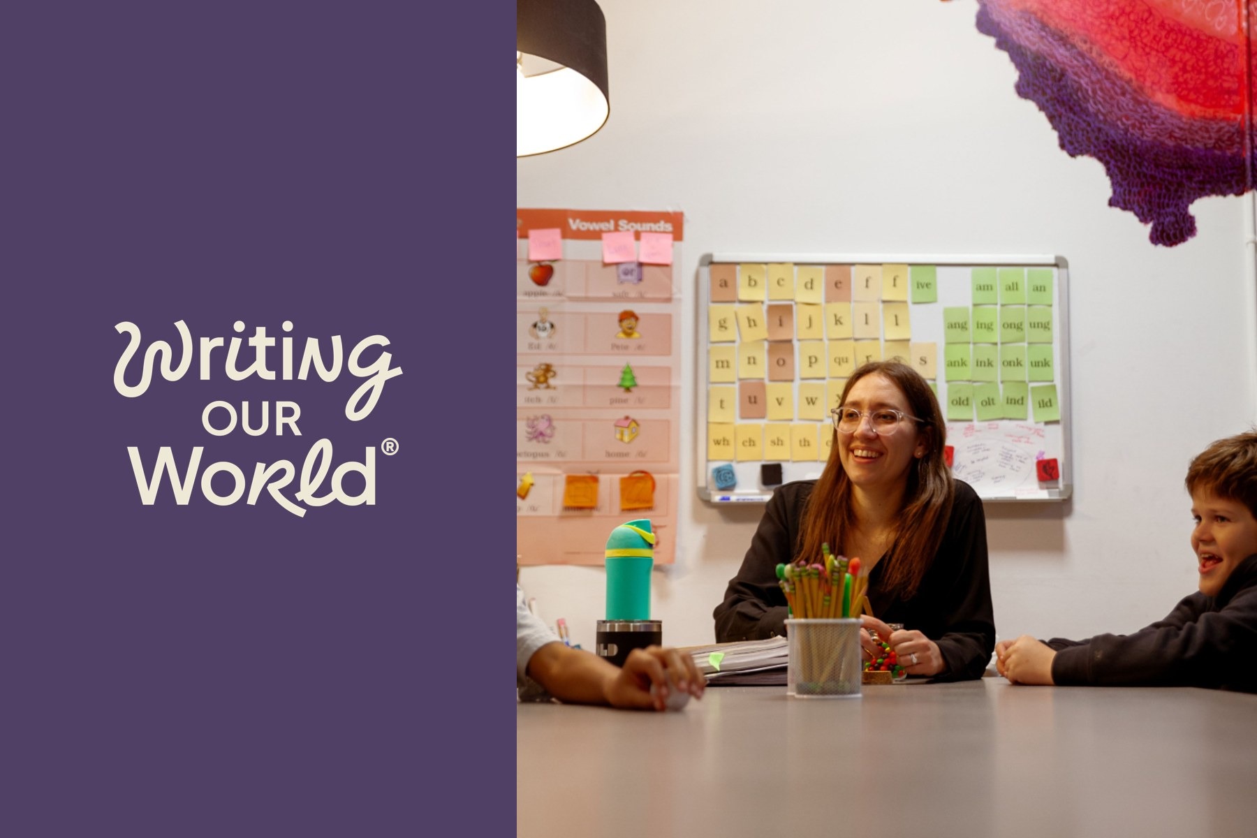 Writing Our World teacher smiling with students at a table