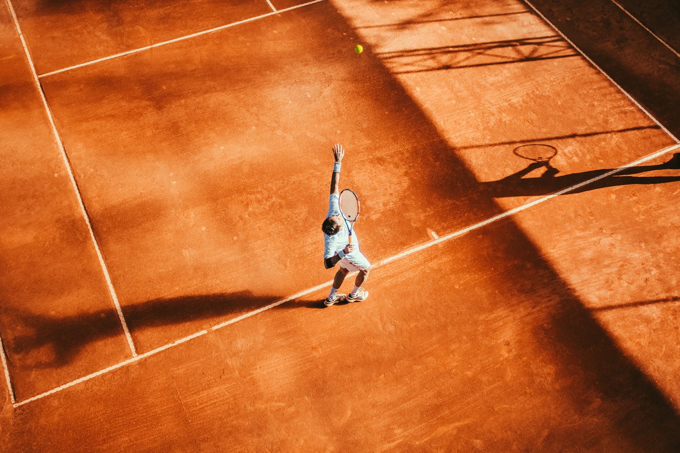 Tennis player reaching up to serve on an outdoor court