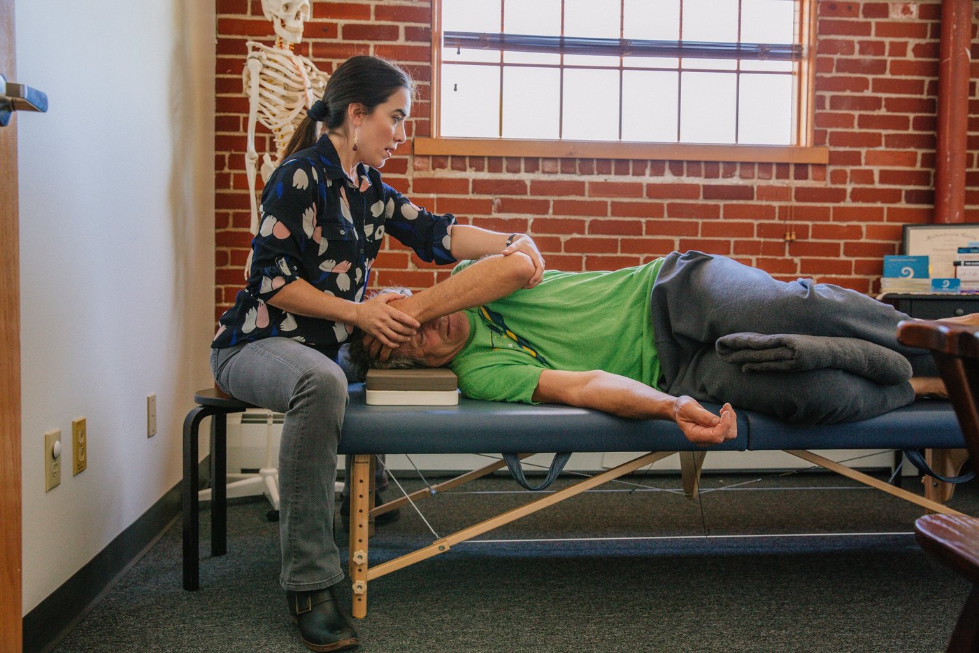 Dayana guiding a client’s arm and shoulder during a side-lying Feldenkrais session