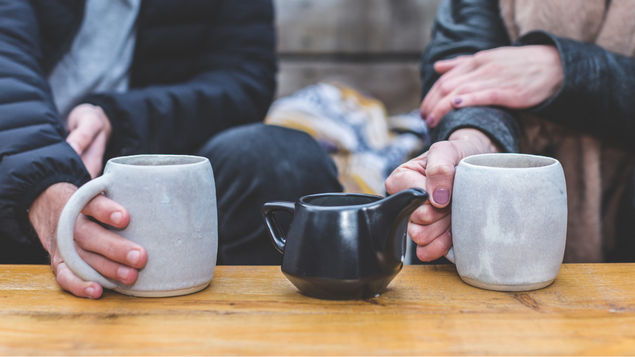 A close up of two people's hands holding tea mugs sitting next to eachother