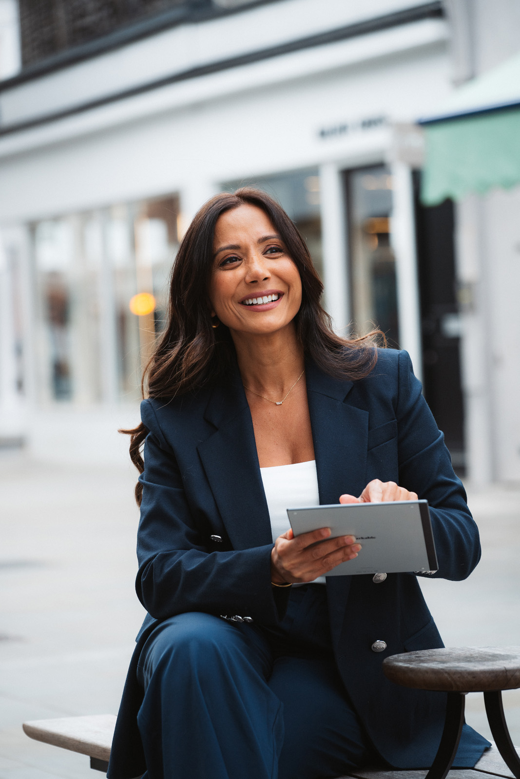 Dr Manrina Rhode smiling, wearing a navy suit and holding a tablet