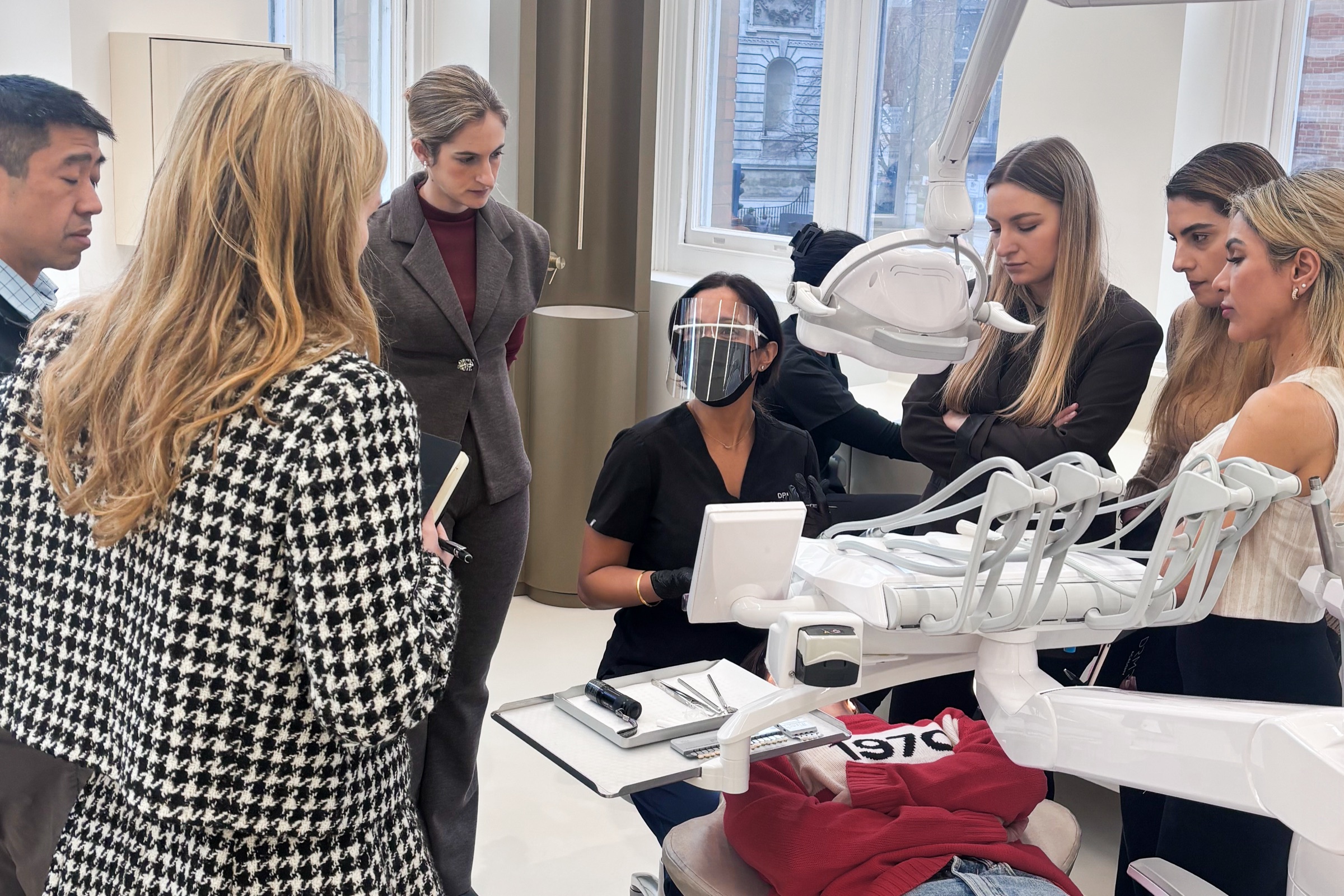 Dr Manrina Rhode teaching at the chair, with dentists gathered round to watch a live veneer case on the September 2026 Designing Smiles course