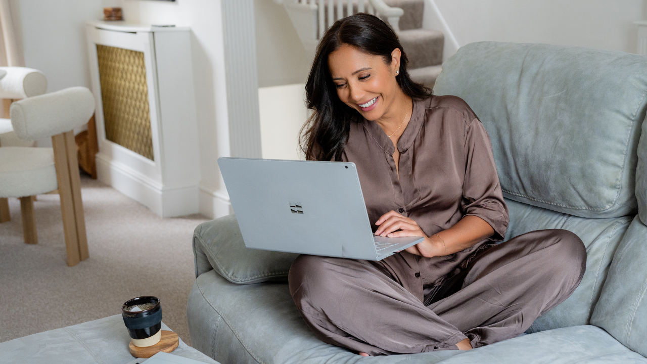 Dr Manrina Rhode sitting cross legged on a sofa, working on a laptop