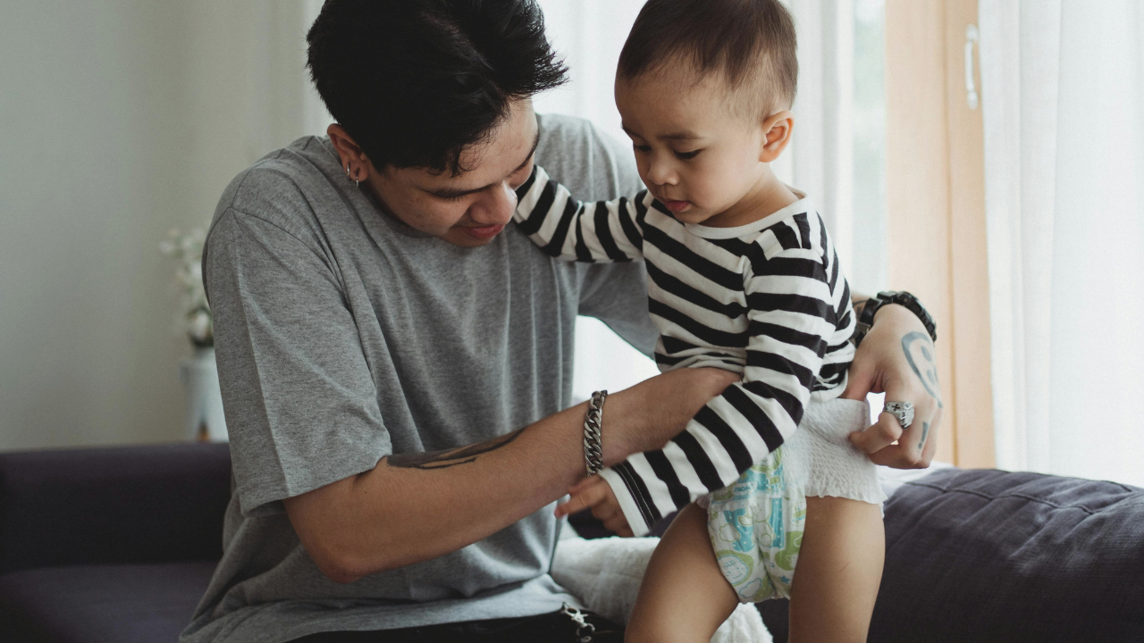 Father is pulling up a nappy onto a potty training toddler