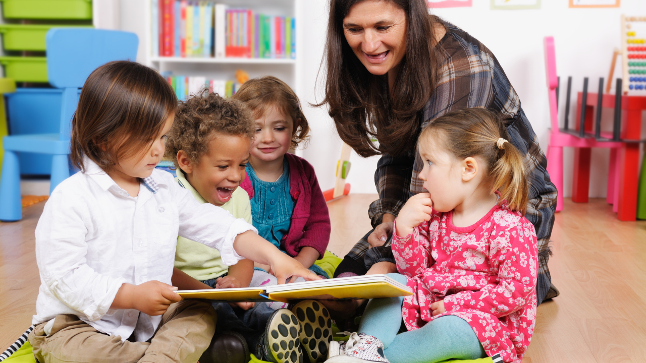 toddlers gather round a book with a childcare worker at nursery