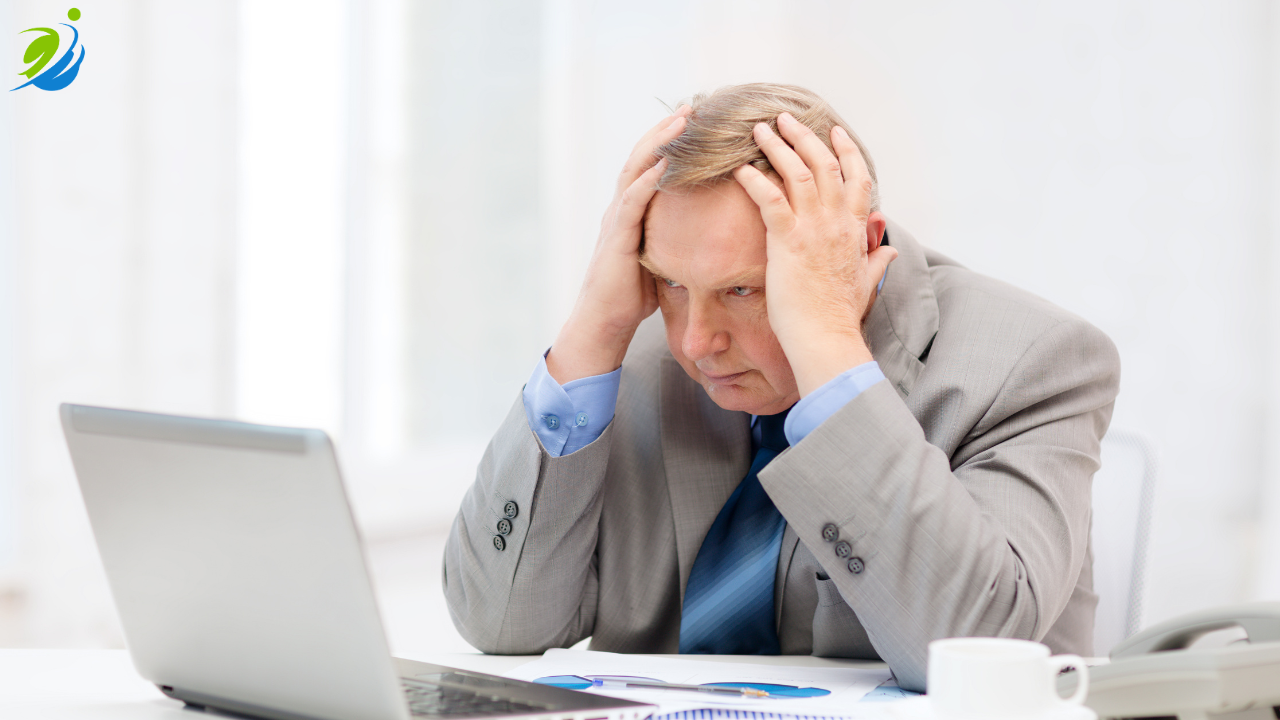 Restaurant owner sitting at a desk holding his head in stress while looking at a laptop, representing the financial strain and long-term cost impact of a workplace injury on a business.