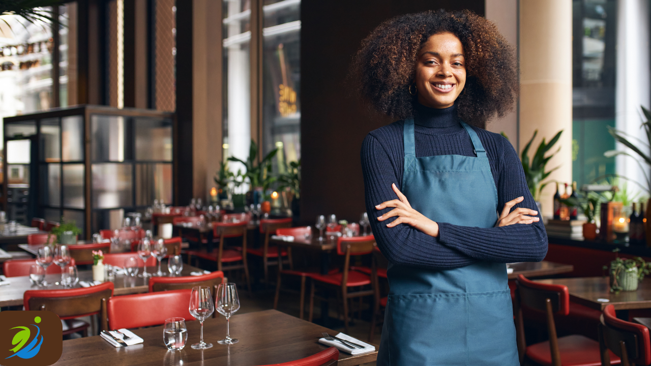Confident restaurant employee standing in a clean, well-organized dining room with arms crossed, representing a culture of safety awareness, professionalism, and consistent operational standards.