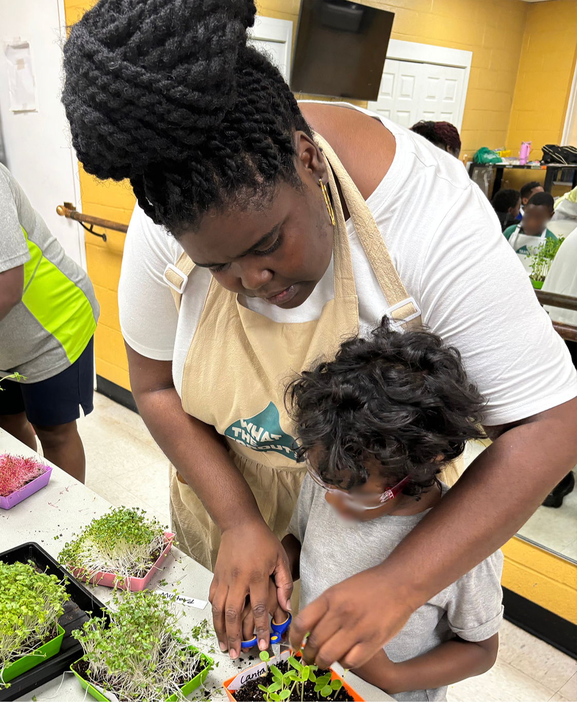 Quandra helping a child harvest microgreens during a hands-on workshop