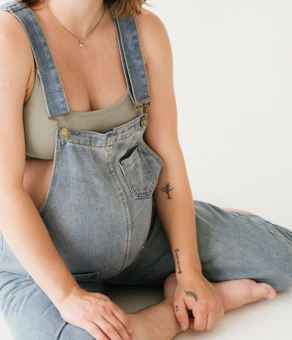 Femme enceinte assise en salopette – conférence gratuite pour réduire les risques de déchirure à l'accouchement