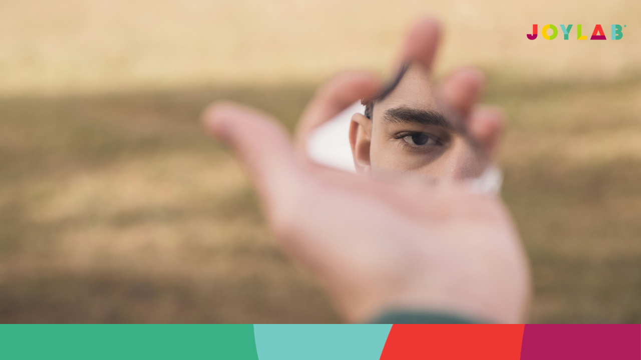Person holding out hand with a small mirror reflecting their eye. 