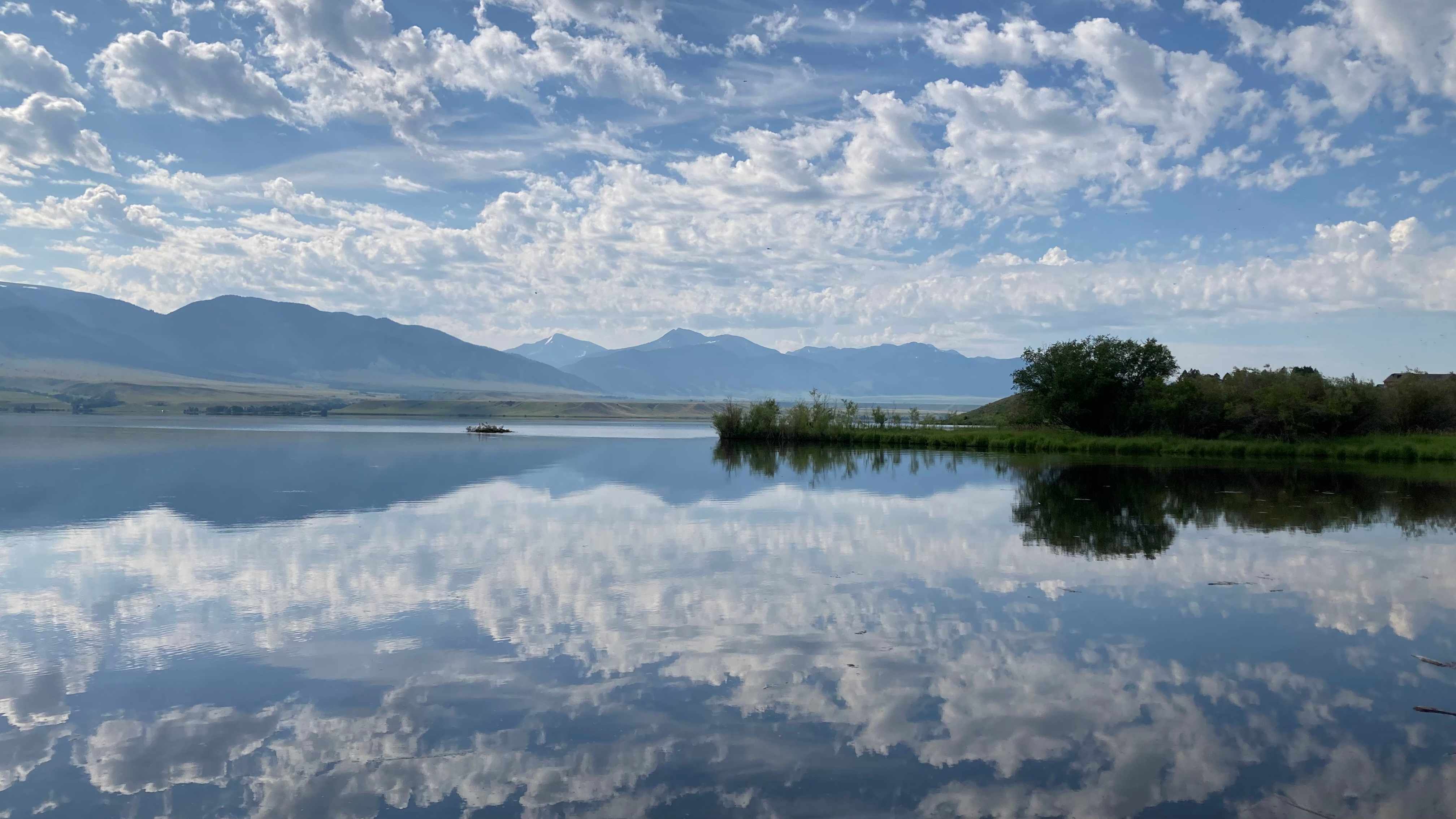 Cloud-filled blue sky reflected in a calm lake with distant mountains, showing cloud perspective and reflections as reference for painting watercolor clouds.