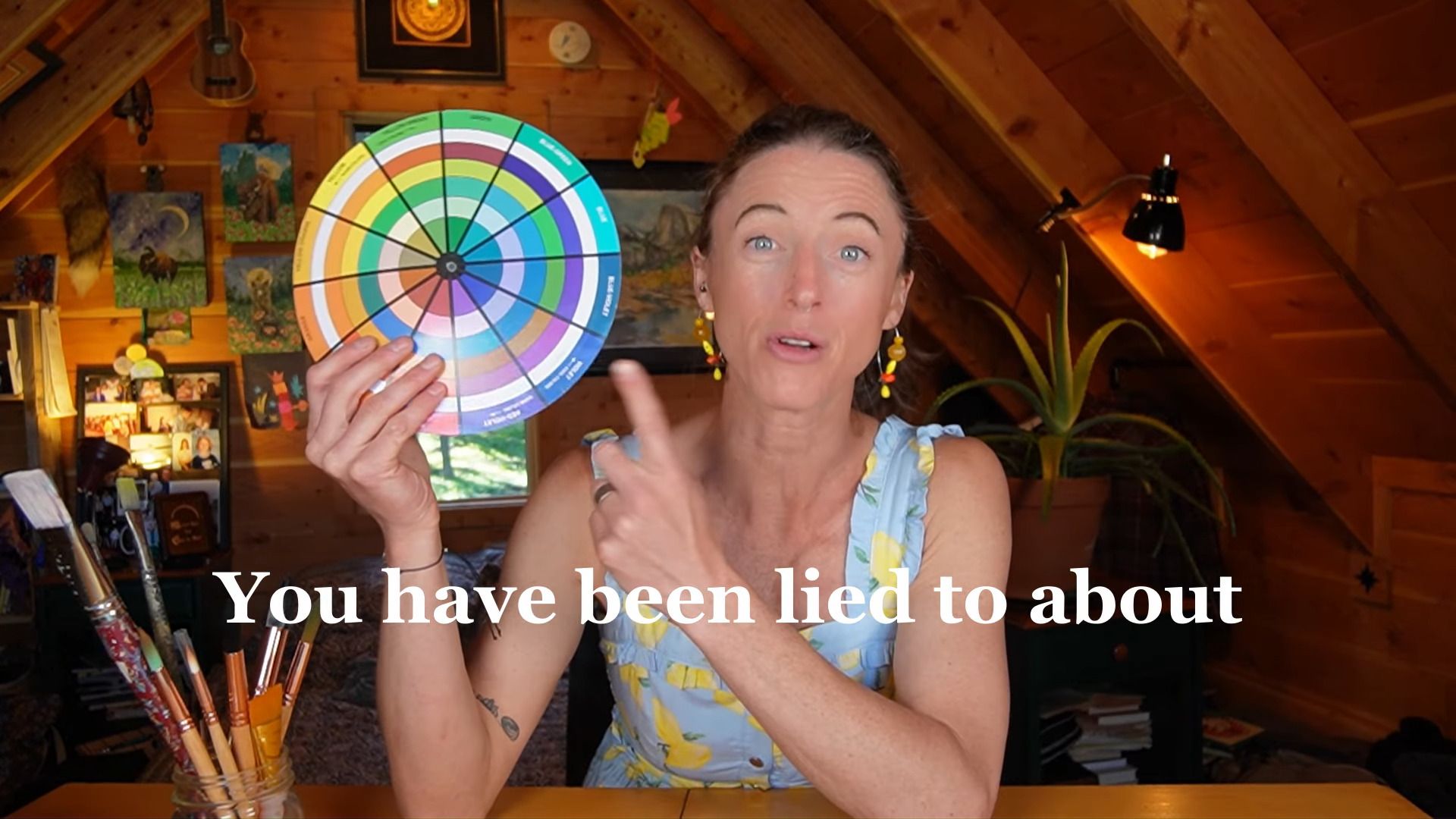 Juliene, a watercolor artist holding a color wheel while explaining CMY and RYB color theory for painters.