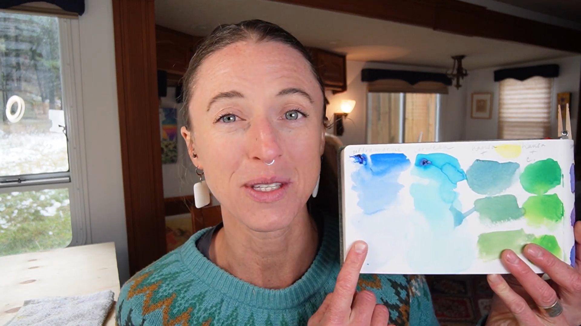 Juliene, a watercolor artist comparing Ultramarine Blue and Cerulean Blue paint swatches in a sketchbook.
