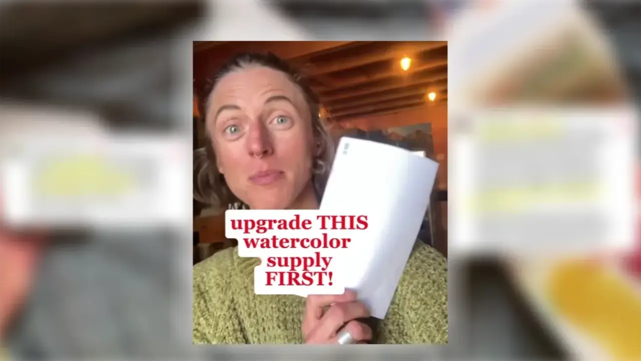 Juliene holds a sheet of watercolor paper, highlighting why upgrading from cellulose to cotton watercolor paper can improve painting results.