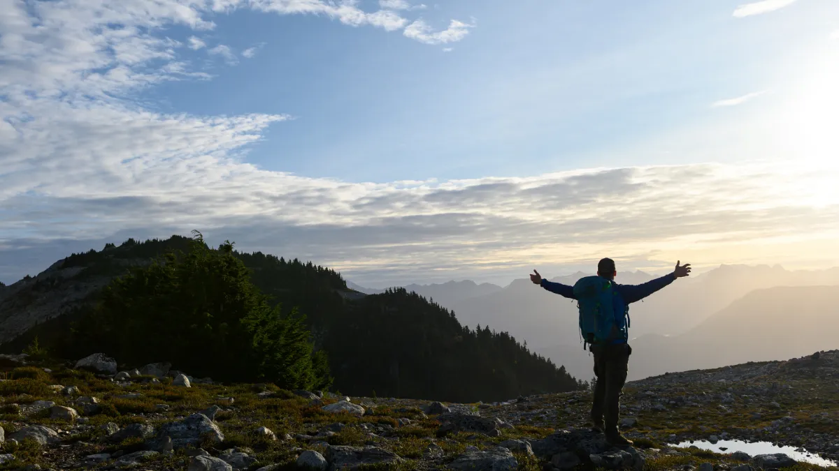A hiker with a backpack standing on a mountain ridge at dawn, arms open wide to the sky