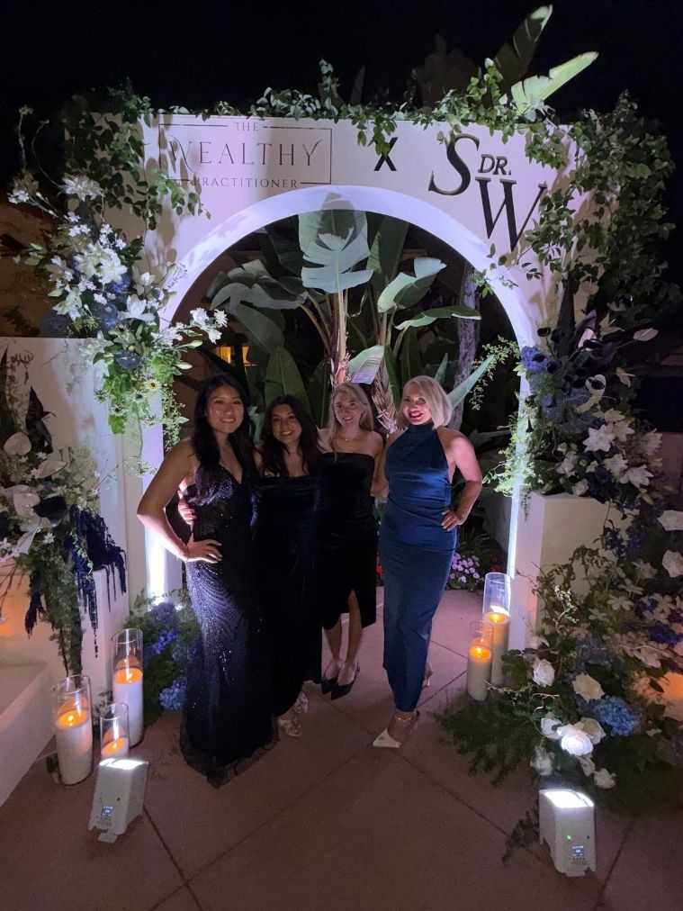 Miranda with three women under a floral arch at a chiropractic coaching event
