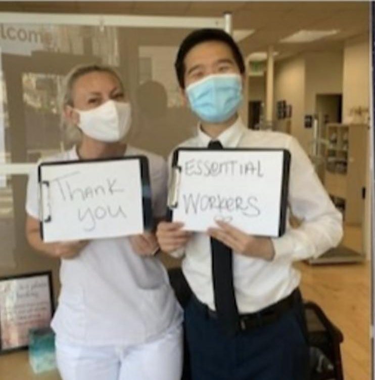 Miranda in a mask holding a Thank you sign next to a coworker holding an Essential Workers sign