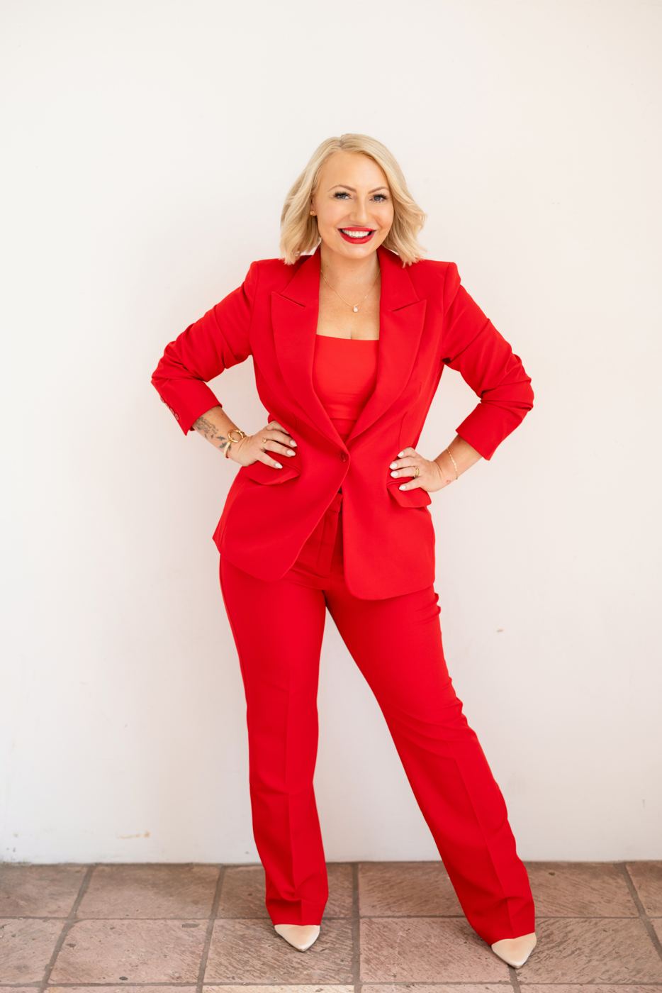 Miranda in a red suit, full length, hands on hips, smiling
