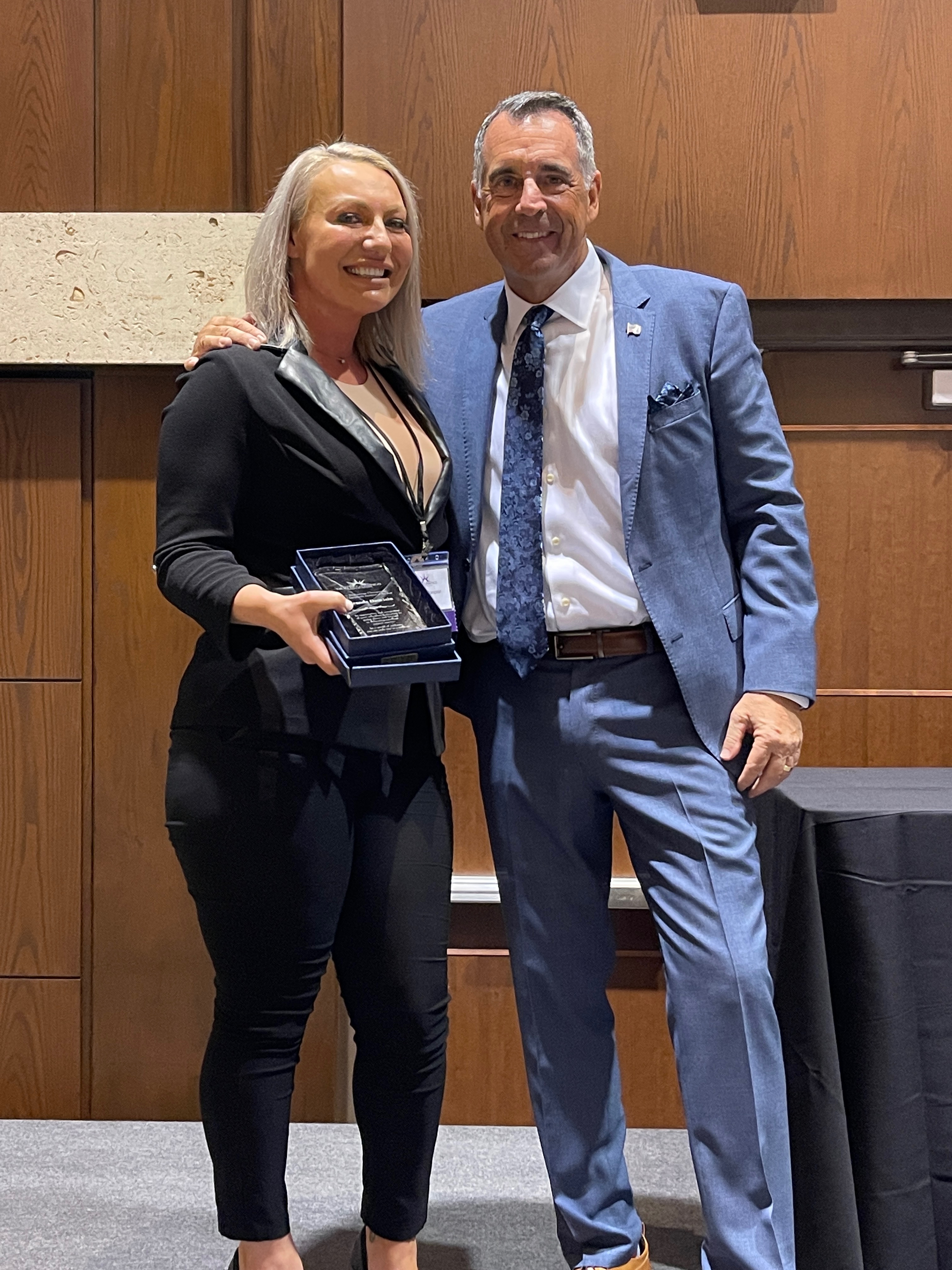Miranda holding a crystal award next to a chiropractic coach in a blue suit