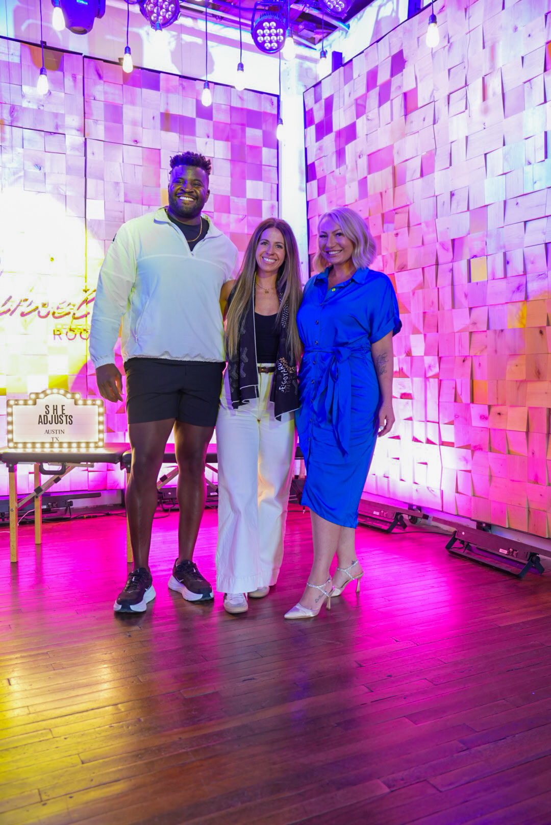 Miranda in a blue dress with two event friends under pink and purple stage lights