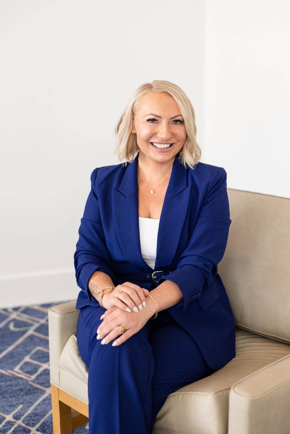 Miranda seated in a cream armchair, hands clasped, smiling warmly